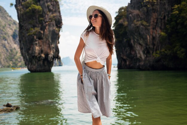 Mujer hermosa joven que viaja en tailandia, vacaciones de verano, estilo casual, gafas de sol, sombrero, falda de algodón, camiseta, sonriente, feliz, aventuras