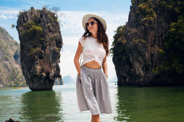 Mujer hermosa joven que viaja en tailandia, vacaciones de verano, estilo casual, gafas de sol, sombrero, falda de algodón, camiseta, sonriente, feliz, aventuras