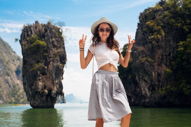 Mujer hermosa joven que viaja en tailandia, vacaciones de verano, estilo casual, gafas de sol, sombrero, falda de algodón, camiseta, sonriente, feliz, aventuras