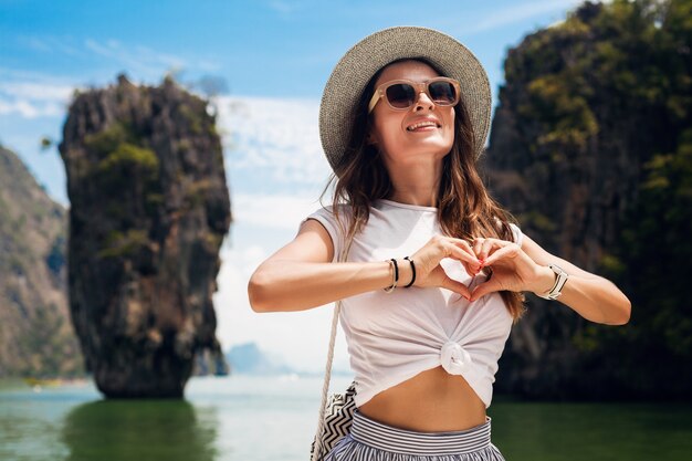 Mujer hermosa joven que viaja en tailandia, vacaciones de verano, estilo casual, gafas de sol, sombrero, falda de algodón, camiseta, sonriente, feliz, aventuras