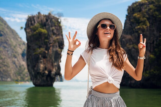 Mujer hermosa joven que viaja en tailandia, vacaciones de verano, estilo casual, gafas de sol, sombrero, falda de algodón, camiseta, sonriente, feliz, aventuras