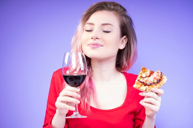 Mujer hermosa joven con una rebanada de pizza y una copa de vino tinto
