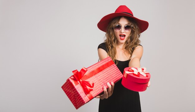 Mujer hermosa joven con regalos, vestido negro, sombrero rojo, gafas de sol, feliz, sonriente, sexy, elegante, cajas de regalo, celebrando, positivo, emocional