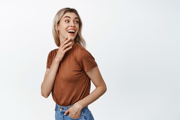 Mujer hermosa joven riendo sonriendo y mirando detrás de su hombro el logotipo del espacio vacío o el texto publicitario de pie sobre fondo blanco