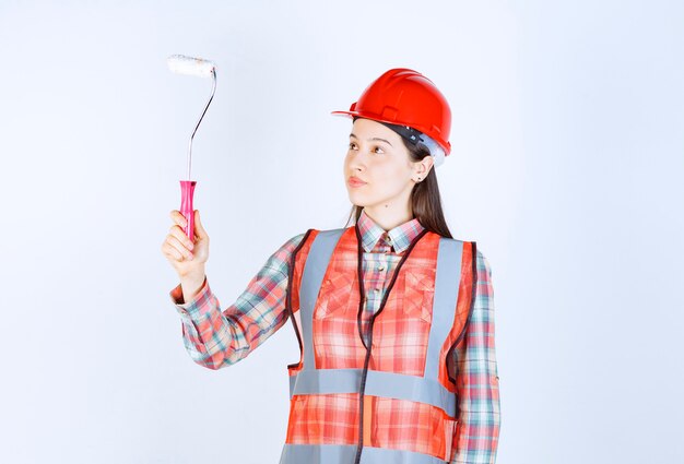 Mujer hermosa joven con un rodillo de pintura para pintar la reparación de la pared.