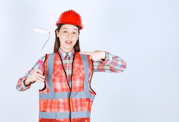 Mujer hermosa joven con un rodillo de pintura para pintar la reparación de la pared.