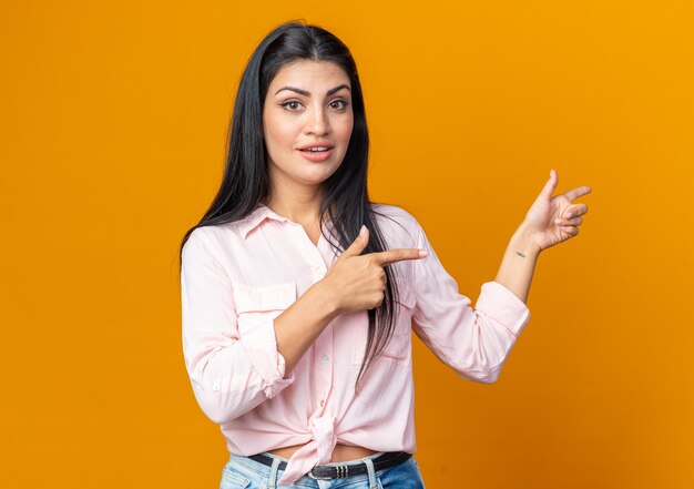 Mujer hermosa joven en ropa casual mirando sonriendo confiado feliz y positivo apuntando con el dedo índice hacia el lado