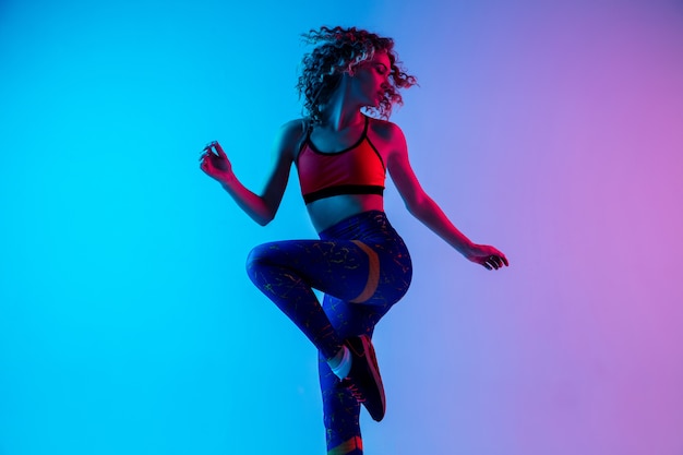 Mujer hermosa joven en ropa deportiva brillante aislada sobre fondo rosa-azul degradado en luz de neón.