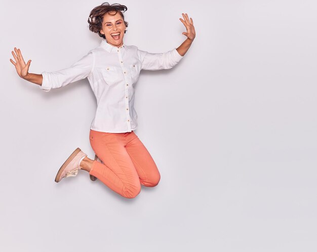 Mujer hermosa joven con ropa informal sonriendo feliz saltando con una sonrisa en la cara y los brazos abiertos sobre un fondo blanco aislado