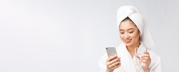 Mujer hermosa joven saludable agua potable belleza cara maquillaje natural con teléfono móvil aislado sobre fondo blanco.