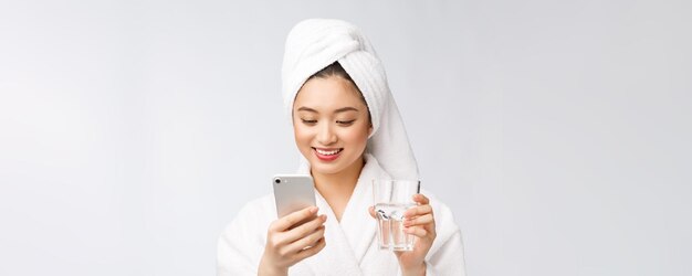 Mujer hermosa joven saludable agua potable belleza cara maquillaje natural con teléfono móvil aislado sobre fondo blanco.