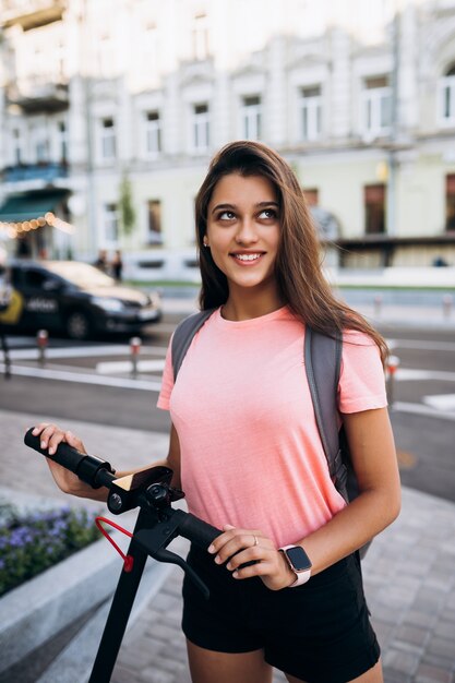 Mujer hermosa joven en un scooter eléctrico, chica moderna en el transporte ecológico.