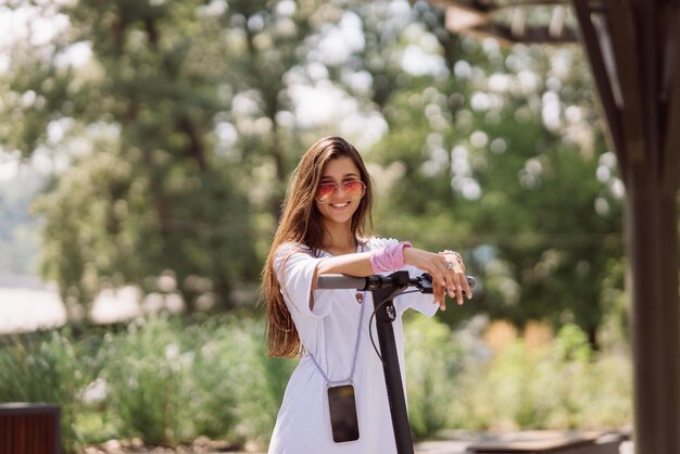 Mujer hermosa joven y scooter eléctrico en el parque