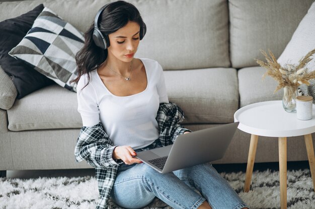 Mujer hermosa joven sentada en casa trabajando en la computadora portátil en los auriculares