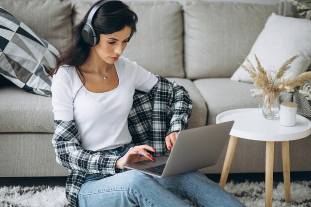 Mujer hermosa joven sentada en casa trabajando en la computadora portátil en los auriculares