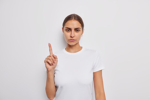 Mujer hermosa joven seria con puntos de cabello oscuro peinado arriba da poses de información en ropa casual aislada sobre la pared blanca