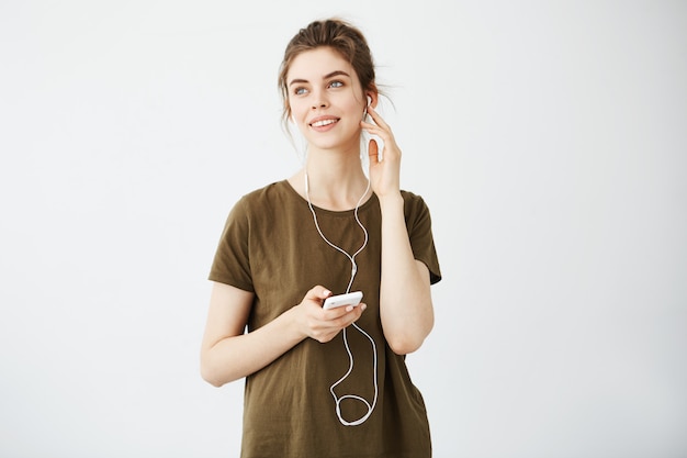 Mujer hermosa joven soñadora que sonríe escuchando música en auriculares