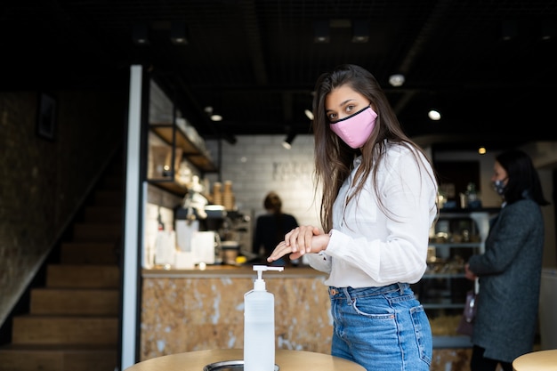 Mujer hermosa joven con sonrisa atractiva en máscara protectora con gel desinfectante de manos para lavarse las manos.