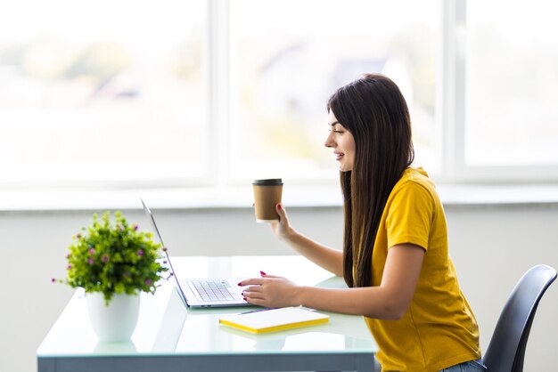 Mujer hermosa joven sosteniendo una taza de café y manteniendo los ojos cerrados mientras se sienta en su lugar de trabajo