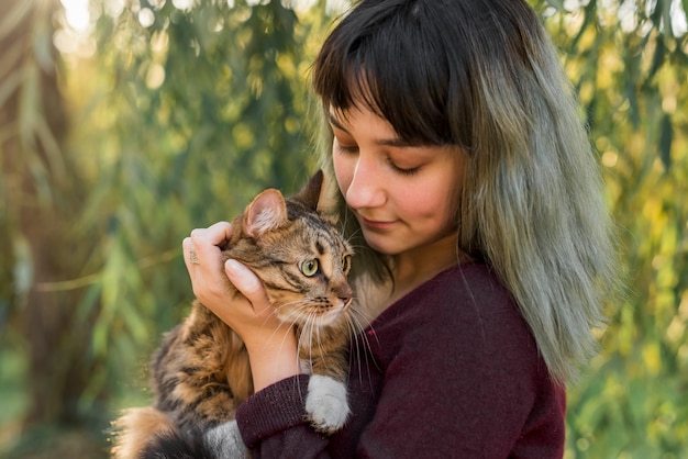 Mujer hermosa joven con su gato de gato atigrado precioso en parque