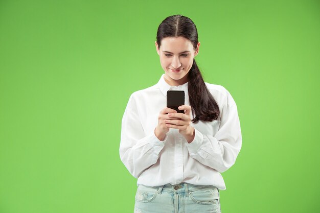 Mujer hermosa joven con teléfono móvil en la pared de color verde. Concepto de emociones faciales humanas.