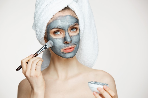 Mujer hermosa joven en toalla en la cabeza que cubre la cara con la máscara sonriendo. cosmetología de belleza y spa.