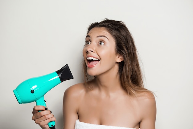 Foto gratuita mujer hermosa joven en toalla cantando con secador de pelo