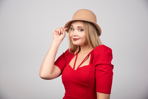 Mujer hermosa joven en vestido rojo tocando su sombrero.