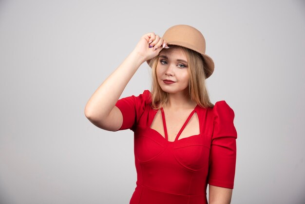 Mujer hermosa joven en vestido rojo tocando su sombrero.