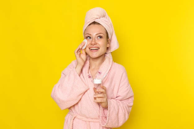 Una mujer hermosa joven de vista frontal en bata de baño rosa limpiando todo el maquillaje con limpiador