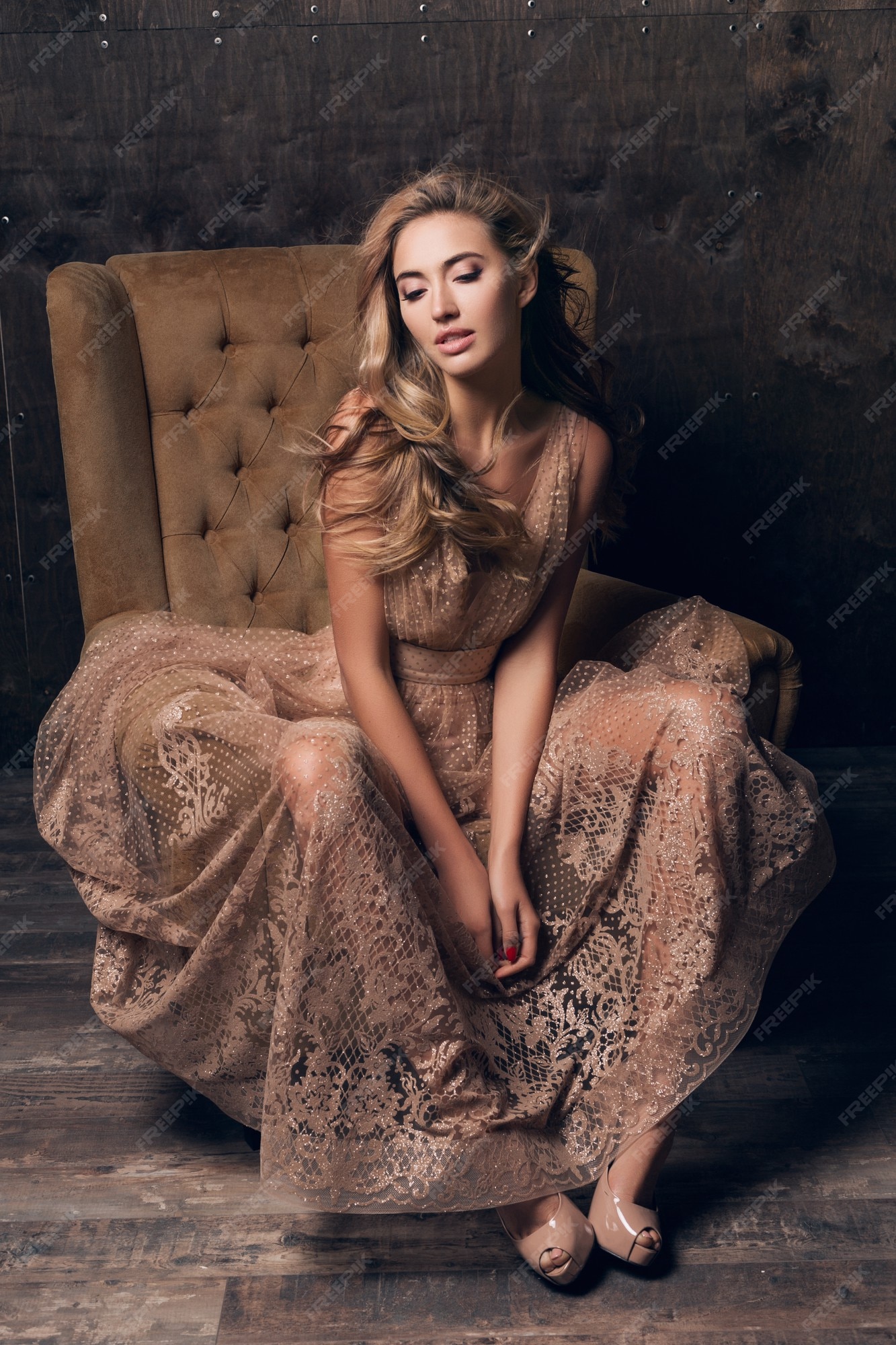 Mujer hermosa modelo sexy en vestido de noche de encaje brillante posando  sentada en una silla de color beige | Foto Gratis