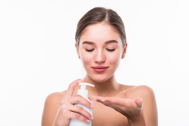 Mujer hermosa y natural joven que sostiene la botella de crema aislada en la pared blanca