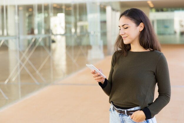 Mujer hermosa positiva enfocada viendo contenido en celular