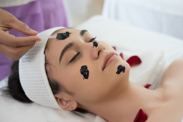 Mujer hermosa que consigue la máscara facial del fango negro en el salón de belleza.