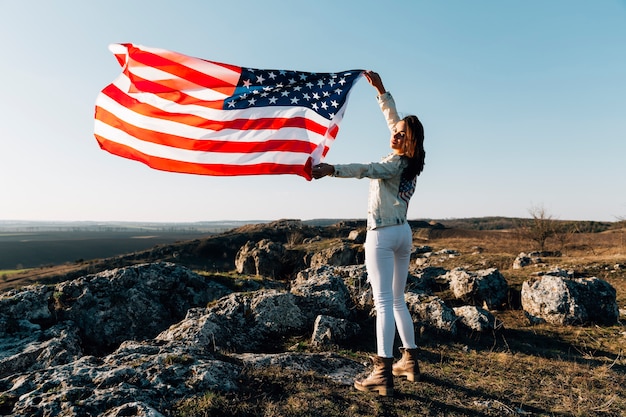 Mujer hermosa que presenta con la bandera americana encima de la montaña