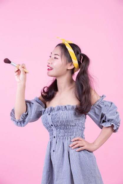 Mujer hermosa que sostiene un cepillo, cepillado en un fondo rosado.