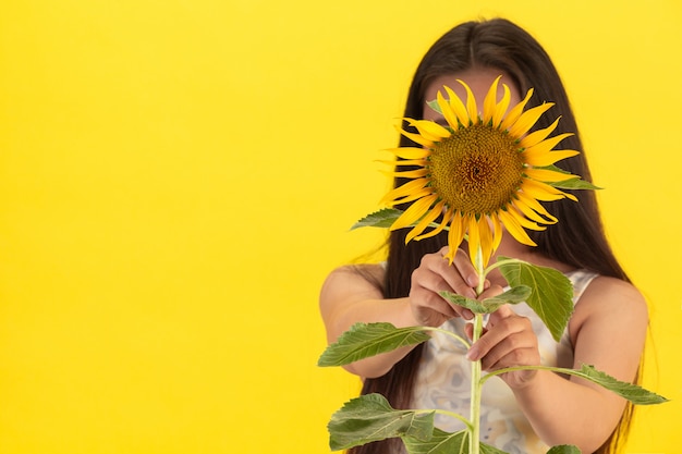 Foto gratuita una mujer hermosa que sostiene un girasol en un fondo amarillo.