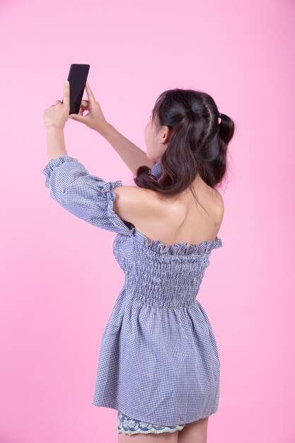 Mujer hermosa que sostiene un smartphone en un fondo rosado.