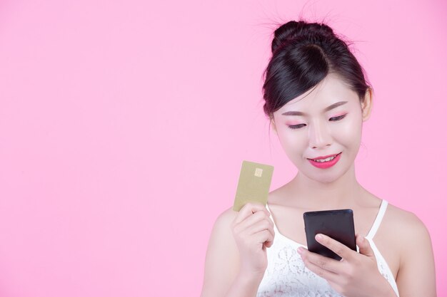 Mujer hermosa que sostiene un smartphone y una tarjeta en un fondo rosado