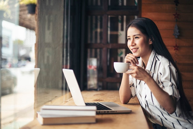 Mujer hermosa que trabaja con el ordenador portátil en el café de la cafetería