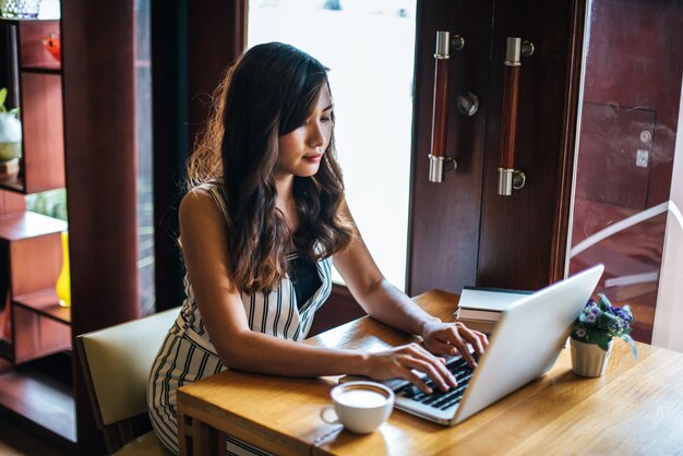 Mujer hermosa que trabaja con el ordenador portátil en el café de la cafetería