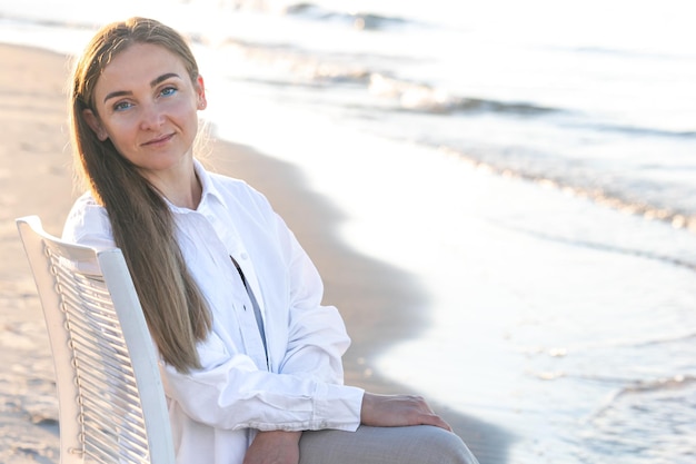 Foto gratuita una mujer hermosa se sienta en una silla cerca del mar.