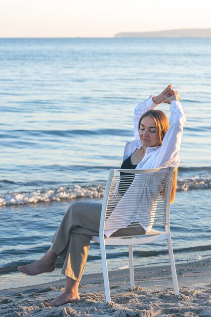 Una mujer hermosa se sienta en una silla cerca del mar.