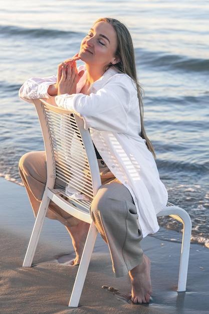 Una mujer hermosa se sienta en una silla cerca del mar.