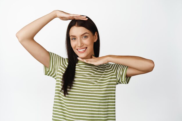 Mujer hermosa sonriente que muestra la cara en el concepto de gesto de caja de mano de cuidado de la piel y rejuvenecimiento de pie sobre fondo blanco