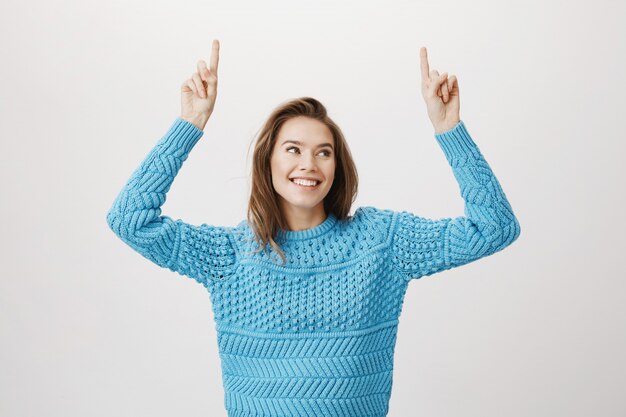 Mujer hermosa sonriente en suéter que señala los dedos hacia arriba