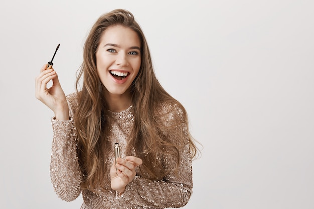 La mujer hermosa sonriente en vestido usa el rimel