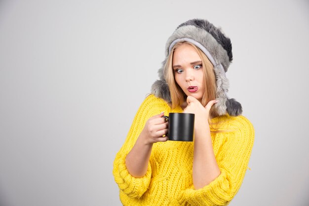 Mujer hermosa en suéter amarillo mirando una taza de té.