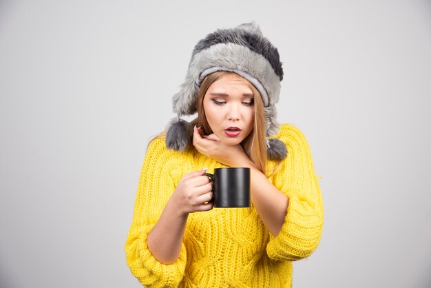 Mujer hermosa en suéter amarillo mirando una taza de té.