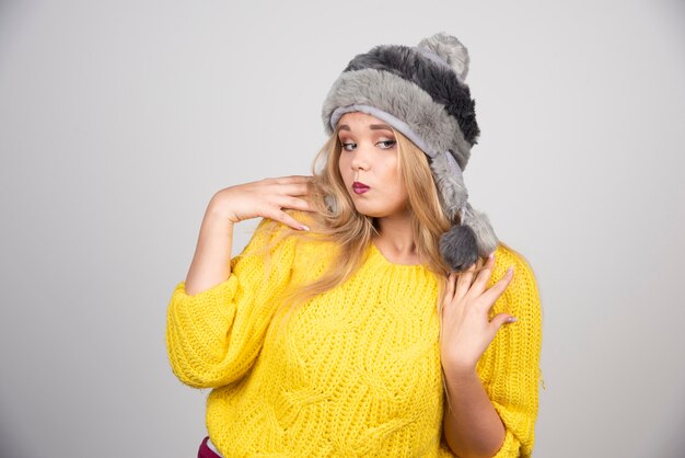 Mujer hermosa en suéter amarillo de pie sobre la pared gris.